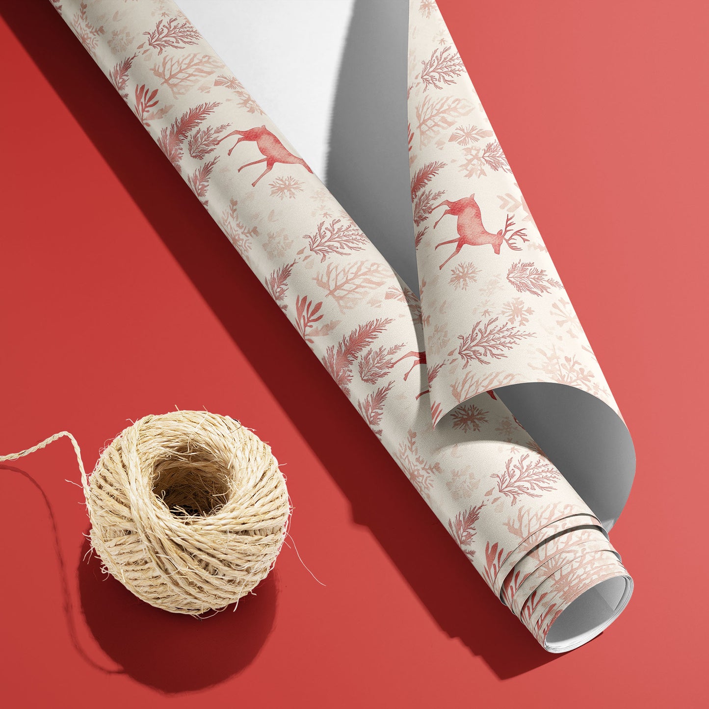 A curled roll of Nordic Wonderland wrapping paper revealing its white underside beside a spool of natural twine on a rich red background.