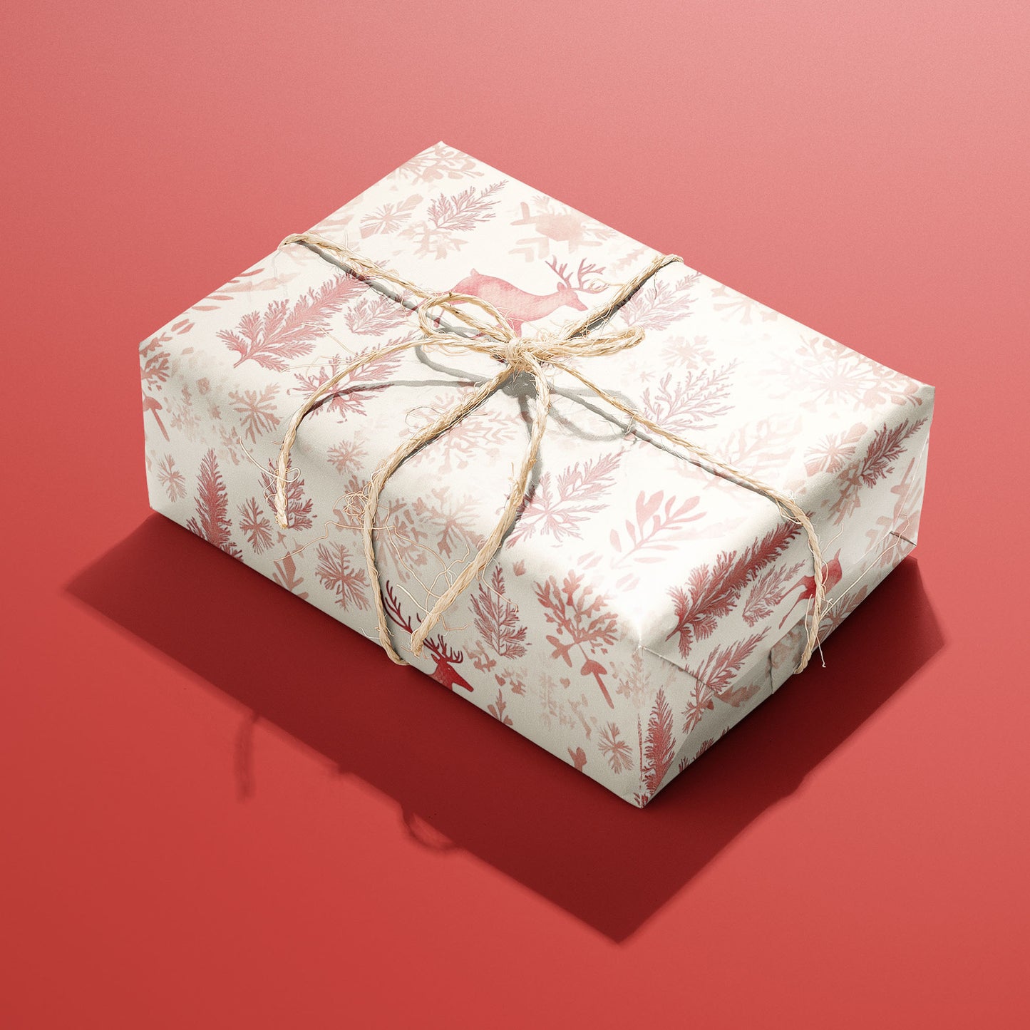 A single box wrapped in Nordic Wonderland paper, patterned with red reindeer and snowy foliage and tied with rustic twine on a red backdrop.