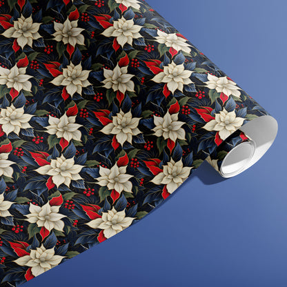 A partially unfurled roll of Elegant Poinsettias gift wrap showing repeating cream poinsettia blooms, red leaves and holly berries on deep navy paper against a soft blue surface.