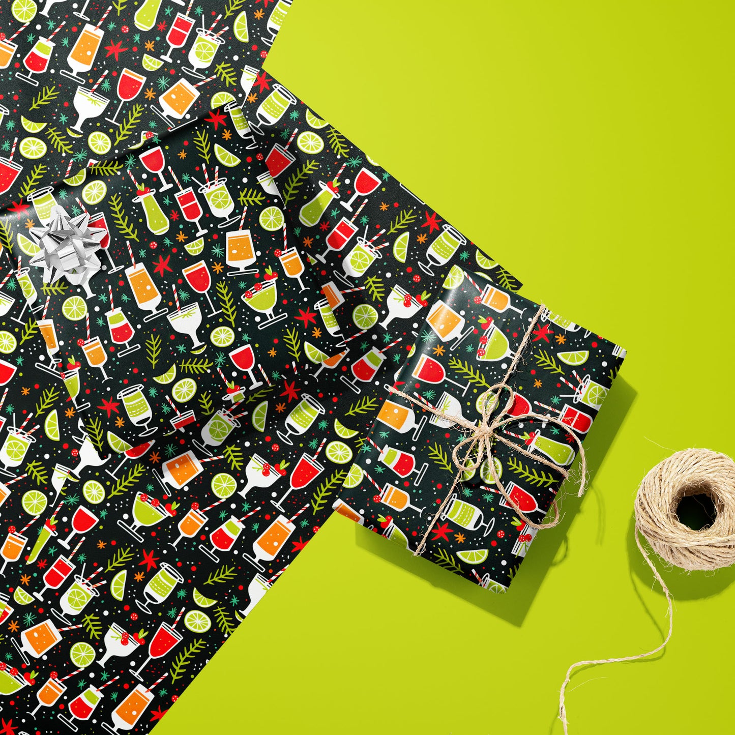 Two gifts wrapped in Christmas Cocktails cocktail-patterned paper, one with a silver bow and one tied with twine, rest on extra sheets beside twine on a lime green surface.