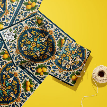 Two gifts wrapped in Citron Azulejo paper—one with a silver bow, one tied in twine—rest on two unused sheets beside a twine spool on a sunny yellow surface.