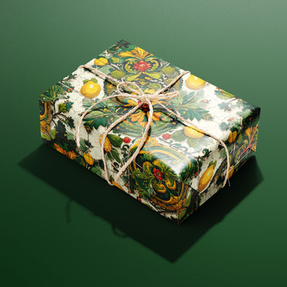 A rectangular gift wrapped in Amalfi Acanthus paper, the lemon-and-acanthus tile design tied with a natural twine bow, set on a deep green background.