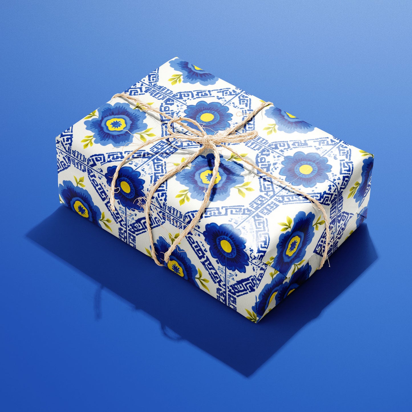 A single box wrapped in Santorini Floriate, its blue floral tile pattern bright on white and tied with natural twine, resting on a saturated blue background.