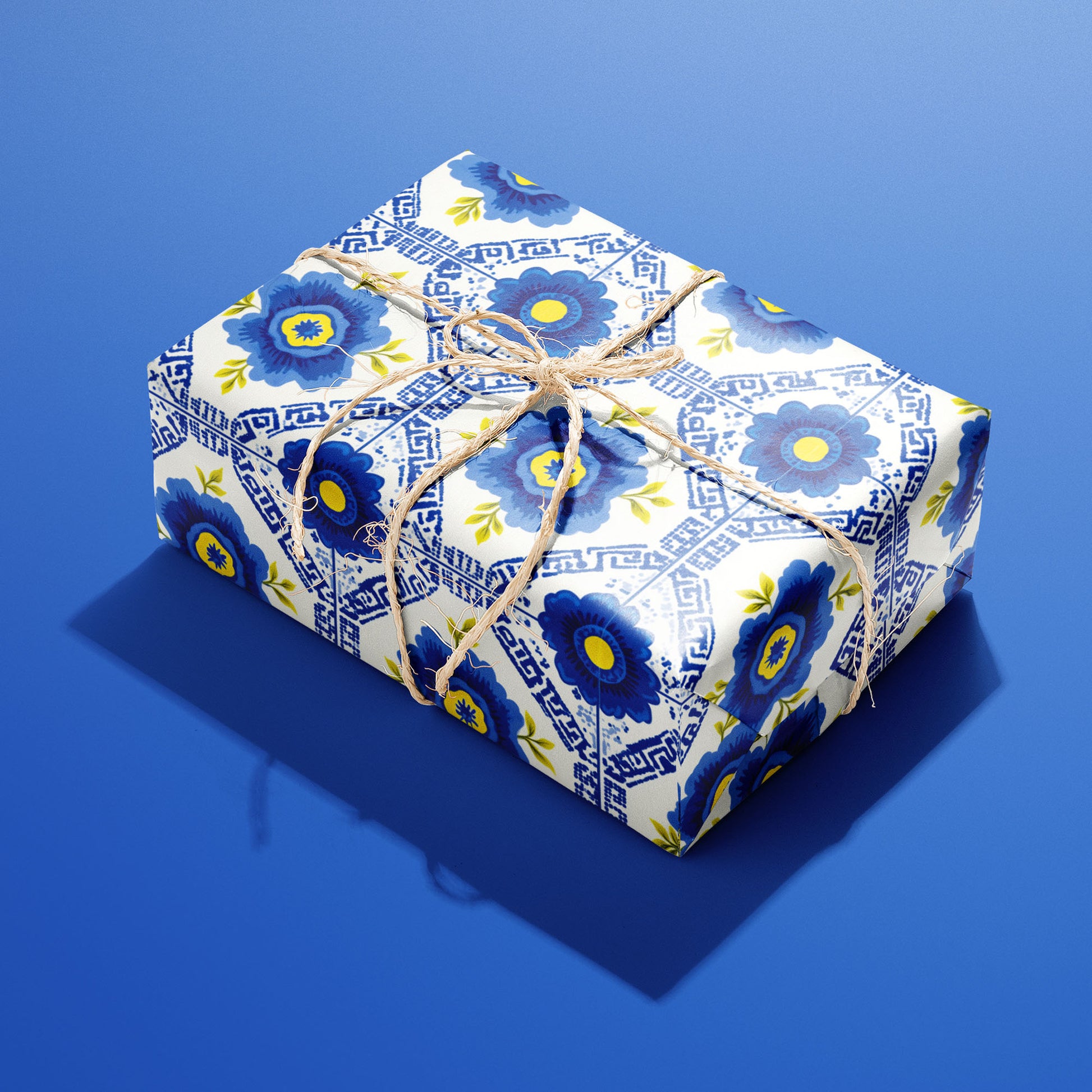 A single box wrapped in Santorini Floriate, its blue floral tile pattern bright on white and tied with natural twine, resting on a saturated blue background.