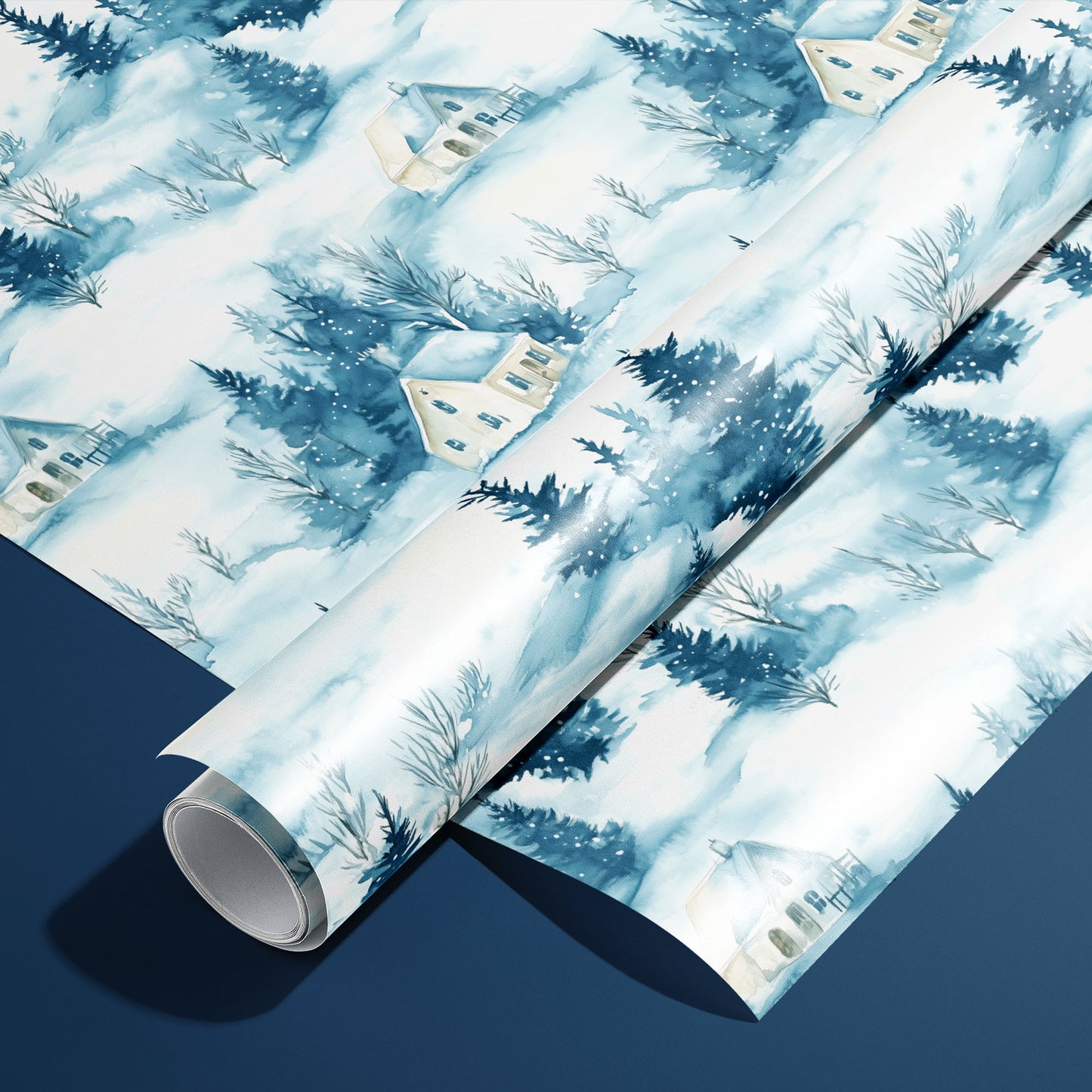 A roll of Cozy Cottage wrapping paper resting on a matching unrolled sheet, featuring watercolor snow-covered cottages and pine trees on soft blue-white against a navy background.