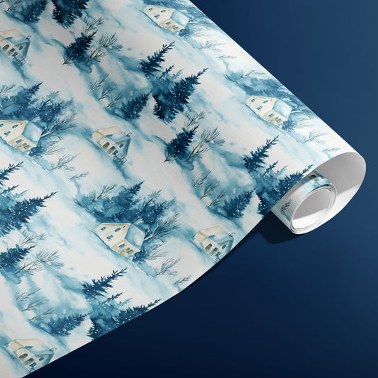 A partially unfurled roll of Cozy Cottage gift wrap showing repeating snowy cottages and evergreen forests in watercolor blues on a deep navy surface.