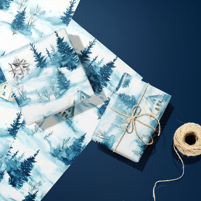 Two gifts wrapped in Cozy Cottage winter-village paper, one topped with a silver bow and one tied with twine, resting on extra sheets beside twine on a navy surface.
