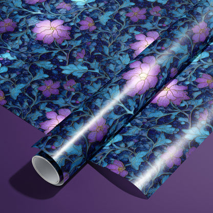 A roll of Lunar Hellebore wrapping paper on an unrolled sheet, showing violet hellebore blooms with teal foliage on midnight blue, set on a deep purple surface.
