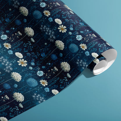 A partially unfurled roll of Midnight Garden wrapping paper showing blue botanical blooms and tiny starry dots on a deep navy ground, on a teal background.