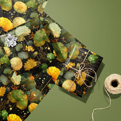 A twine-tied gift in Nocturne Herbarium rests on two unused sheets with a silver bow nearby and a twine spool, showing botanical collage motifs on a black ground over an olive green surface.