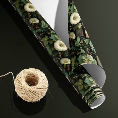 A partially unfurled roll of Vesper Botanica with its white underside visible beside a spool of natural twine, the vintage floral and lunar print on black set on a dark olive green surface.
